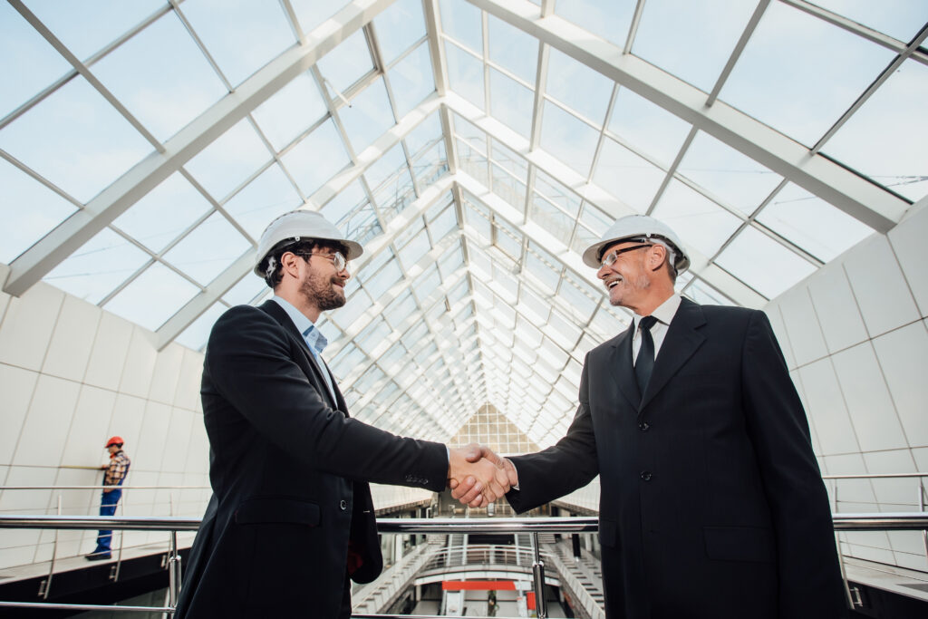 two cheerful businessman handshaking in helmet at new building.